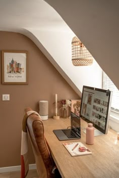 an open laptop computer sitting on top of a wooden desk under a slanted ceiling