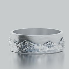 a silver ring with mountains in the middle and water on it's sides, against a gray background