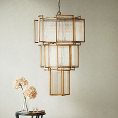 a chandelier hanging from the ceiling over a table with flowers on it next to a vase