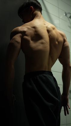 a man standing in front of a shower with his back turned to the camera and no shirt on