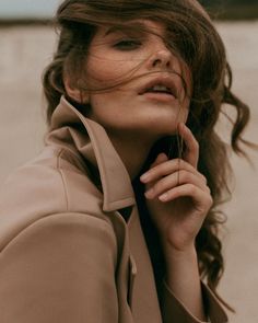 a woman in a trench coat is holding her hand to her ear and looking off into the distance