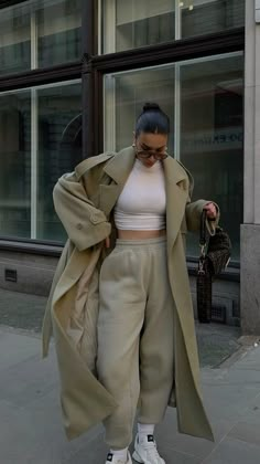 a woman is walking down the street in high heels and a trench coat over her shoulders