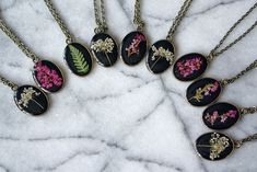 These sweet oval pendant necklaces feature three options of pressed botanicals atop a black background for a real pop! Choose your favorite at check out: Heather, Queen Anne's Lace, Fern Each pendant and chain is antique bronze. Black Flower Necklace For Gift, Black Nature-inspired Necklace For Gift, Black Round Pendant Necklace Nature-inspired, Black Pressed Flowers Jewelry Gift, Botanical Resin, Heather Flower, Pressed Fern, Megan Brown, Pressed Botanicals