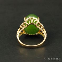 A statement piece that is bound to bring a vibrant and energetically enhanced essence to your days, this Statement Nephrite Jade Ring is both classic and contemporary. The center stone is a natural, untreated AAA nephrite jade stone of a statement-sized 11.75 carats, set in a four prong setting. With intricate details featuring 0.07 carats of sparking white diamonds on either side of the stone, this piece is set in a warm 18kt rose gold setting. Dimensions: Center Stone: Natural, untreated AAA N Elegant Green Opal Ring In 14k Gold, Elegant Green Opal Oval Ring, Elegant Oval Chrysoprase Rings, Elegant Green Gemstones In 14k Gold, Formal Yellow Gold Chrysoprase Jewelry, Elegant Green Round Gemstones, Elegant Gold Jade Ring, Elegant Emerald Jade Ring With Cabochon, Elegant Chrysoprase Emerald Ring For Anniversary