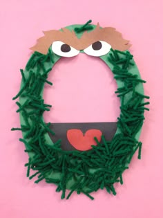 a green wreath with eyes and a red heart in the center on a pink background