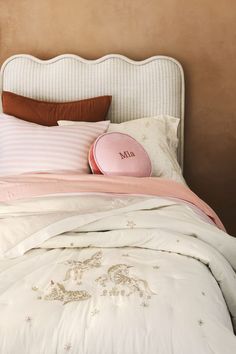 a white bed with pink and brown pillows on it's headboard next to a beige wall