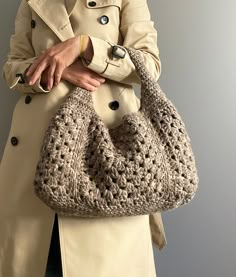 a woman wearing a trench coat holding a crocheted purse