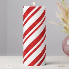 a red and white striped candle sitting on top of a table next to a vase