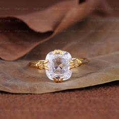 an oval cut white diamond ring with gold accents on top of a leafy surface