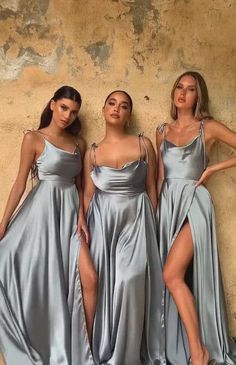 three women standing next to each other wearing silver dresses and one has her leg high