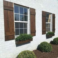 three windows with wooden shutters on the side of a white brick building