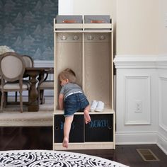 a toddler is sitting in a wooden locker with chalk writing on the bottom and feet