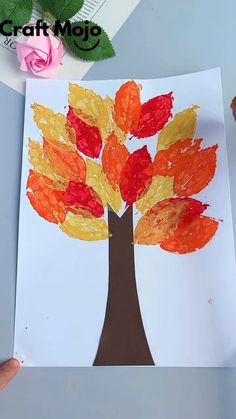 a child's hand holding up a piece of paper that has been made to look like a tree