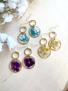 six different earrings with flowers in them sitting on a table next to some white flowers