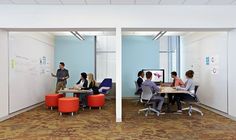 several people are sitting at desks in an office with whiteboards on the walls