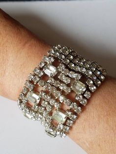 "This Vintage Hollywood Glam Bracelet features ten length of chaton-cut clear rhinestones with 3 vertical columns at the center. The center has six squares with large clear crystals. On one side is a square hinged fold over box clasp. The base metal is plated in Rhodium with exquisite workmanship. This lovely cuff is from Circa; 1950 and is in excellent vintage condition with all rhinestones intact with none missing. Our jeweler has soldiered several squares to keep it from the landfill. If you Arm Candy Bracelets, Bridal Cuff, Candy Bracelet, Hollywood Glam, Holiday Jewelry, Wide Cuff, Rhinestone Bracelet, Vintage Hollywood, Hollywood Glamour