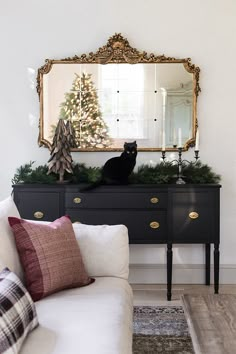 a black cat sitting on top of a dresser next to a christmas tree and mirror