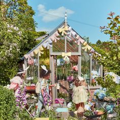 two girls are standing in front of a small greenhouse with flowers and bunting on it