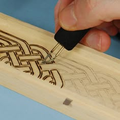 a person using a wood carving tool on a piece of wood with an intricate design