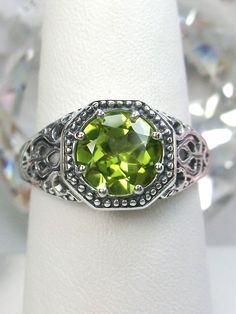 Natural Peridot RingNew Vic Design#D11 Inspired by Victorian and Edwardian designs, this stunning antique reproduction ring is crafted in white gold. This gorgeous ring is set with a flawless round natural peridot. The stunning gemstone is 8mm in diameter. The band is marked 925 (sterling silver),10k or 14k as chosen. Notice the beautifully intricate design of the silver filigree setting and band. The delicate swirl filigree craftsmanship travels down the band and morphs into angular accents. Th Classic Peridot Jewelry With Accent Stones, Antique Green Promise Ring, Classic Peridot Rings With Prong Setting, Classic Peridot Jewelry With Prong Setting, Classic Round Cut Peridot Jewelry, Victorian Green Ring With Center Stone, Heirloom Peridot Jewelry For Anniversary, Classic Green Filigree Ring With Gemstone, Antique Green Rings With Prong Setting