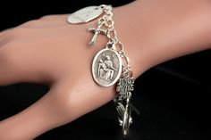 "A Pieta medal combined with a collection of silver plated Christian theme charms have been dispersed around a shimmering silver plated bracelet chain in this handmade charm bracelet. This religious charm bracelet is then completed with a lobster clasp and a 1/2 inch of chain at the end for adjustable sizing. ● Bracelet Styles ● Style #1 - Charms in this bracelet include a \"Christ Carrying the Cross\" charm, praying hands charm, a \"So Very Blessed\" charm, a Jesus fish charm, a \"Jesus loves y Symbolic Silver Rosary Bracelet For Gifts, Symbolic Silver Rosary Bracelet Gift, Silver Symbolic Rosary Bracelet As Gift, Symbolic Silver Rosary Bracelet, Spiritual Silver Rosary Bracelet With Charms, Silver Rosary Bracelet With Charms As Gift, Vintage Silver Rosary Bracelet As Gift, Nickel Free Silver Rosary Bracelet For Gift, Engraved Silver Rosary Bracelet As Gift