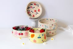 four bowls with fruit painted on them are sitting next to a white wall and an object in the background