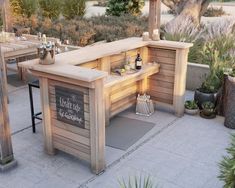 an outdoor bar is lit up with candles and bottles on the outside patio area, surrounded by potted plants