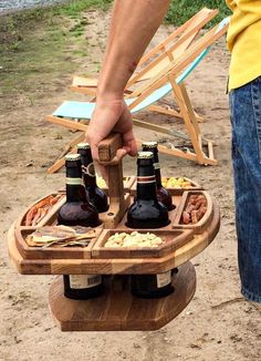 a man is holding two beer bottles on top of a picnic table with food and drinks in it