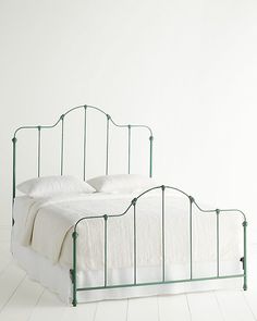 a green metal bed frame with white sheets and pillows on it, against a white wall