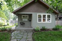 a small gray house sitting on top of a lush green field