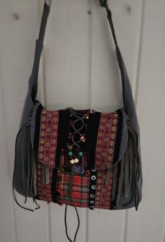 A pair of dungarees transformed into a rugged, distressed boho bag, with a worn look. Featuring fringes made from leather and suede.  Vintage trims, ribbons, pieces of suede, leather and buttons, beads.  Great festival/art bag Interior:  One zipper pocket, one slip pocket Exterior: One slip pocket Top closure:  Magnetic snap Size: 17″ long x 12.5″ tall x 2″ deep (approx) shoulder bag or cross body bag gunmetal hardware Adjustable strap Bohemian Fringe Hobo Shoulder Bag, Artisan Shoulder Bag With Fringe For Festivals, Bohemian Upcycled Tote Shoulder Bag, Artisan Fringe Shoulder Bag For Festival, Festival Handmade Hobo Satchel Bag, Handmade Festival Hobo Satchel Bag, Bohemian Satchel With Adjustable Strap, Brown Bohemian Satchel With Fringe, Bohemian Brown Fringe Satchel