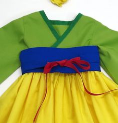 a yellow and blue dress with red ribbon on the waist, sitting on top of a white surface