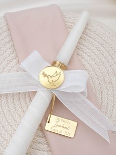 a pink blanket with a white ribbon and a gold name tag on it, next to a candle