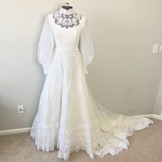 White Lace Embroidered Mock Neck Wedding Gown. Mock Neckline With Sheer Lace Upper And Embroidered Florals. Long, Sheer Puffed Sleeves With Embroidered Button Snap Cuffs. Gathered Waist, A-Line Silhouette, Back Zipper Closure. There Is No Size Listed Measurements - Shoulder To Shoulder 14.5", Pit To Pit 15.5", Waist 12.5" Pit To Wrist 19", Shoulder To Wrist 24", Hip 27" No Major Flaws, Stains, Marks Or Holes Tags: Wedding, Gown, Dress, Victorian, Romantic, Cottage Core, Bohemian, Lace, Fashion Wedding Dresses 70s Style, German Wedding Dress, Edwardian Wedding Dress, Wedding Dresses 60s, 20s Fashion Dresses, 1920s Wedding Dress, Short Wedding Gowns, Vintage Wedding Dress Boho, Edwardian Wedding