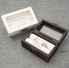 an open wooden box with two wedding rings in it sitting on the floor next to another box