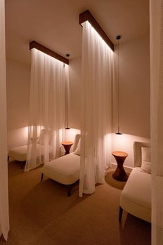 a room with three beds and two lamps on either side of the bed are white drapes hanging from the ceiling