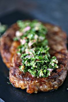 a piece of meat covered in greens on top of a black plate