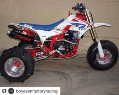 a red, white and blue dirt bike parked in front of a wall with wheels