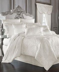 a bed with white comforter and pillows in a room next to a table on hardwood flooring