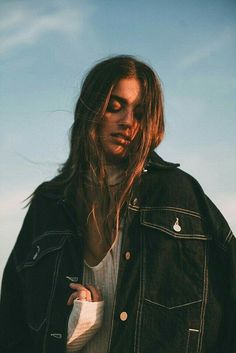 a man with long hair wearing a jean jacket and holding a skateboard in his hand