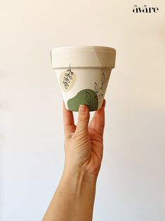 a hand holding up a cup that is decorated with leaves and berries on the side