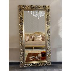 a large gold framed mirror sitting on top of a wooden floor next to a couch