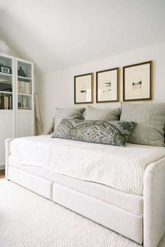 a white daybed with pillows and pictures on the wall above it in a bedroom