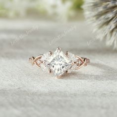 a close up view of a ring with a princess cut diamond surrounded by three smaller diamonds