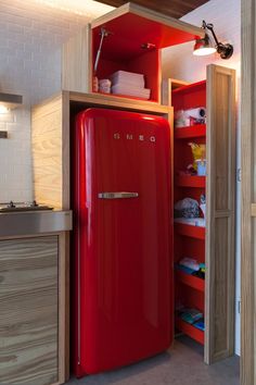 a red refrigerator sitting inside of a kitchen next to a sink and cupboard filled with items