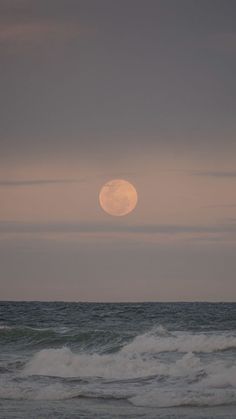 the moon is setting over the ocean waves