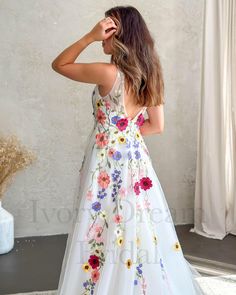 the back of a woman wearing a white dress with colorful flowers on it, standing in front of a wall