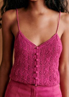 a close up of a woman wearing a pink tank top and high waist pants with buttons