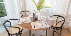 a dining room table set for four with place settings and plates on it, in front of an open window