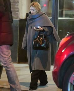 a woman is walking down the street with her cell phone in her hand while wearing a gray coat and black tights